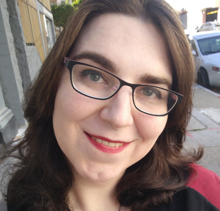 April “Kit” Walsh, a white woman with shoulder length hair, smiles at the camera. The bottom of the headshot suggests that she is wearing a Star Trek uniform.g